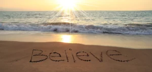 Believe written on a beach at sunset.